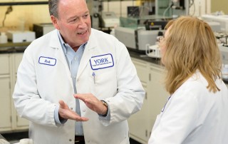 Two YORK Labs employees having a discussion in a laboratory while wearing white lab coats